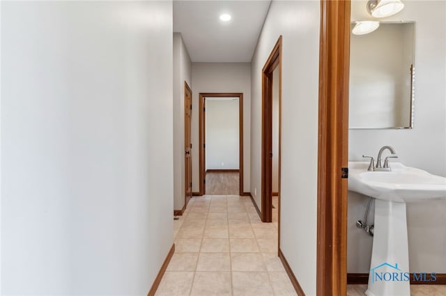 corridor with light tile patterned floors, a sink, and baseboards