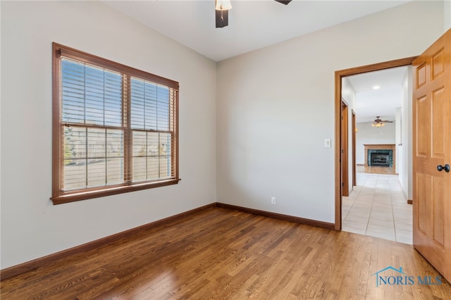 empty room featuring light wood finished floors, ceiling fan, a fireplace, and baseboards