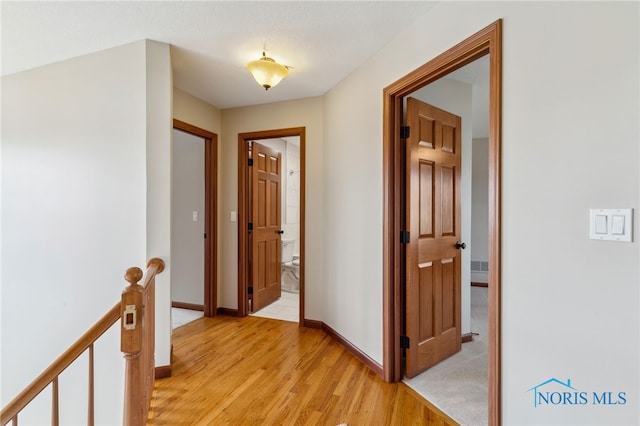 corridor featuring light wood-style flooring, an upstairs landing, and baseboards