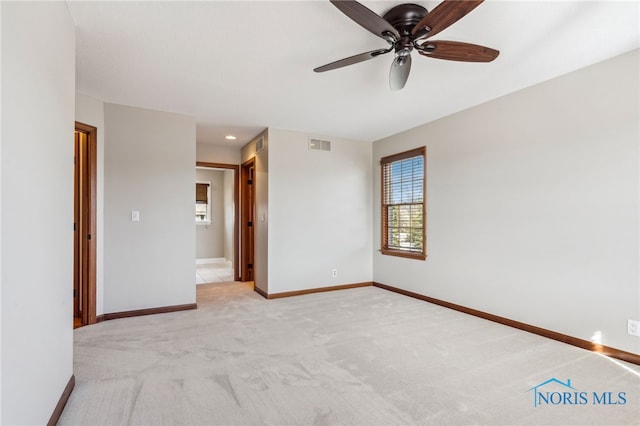 spare room with light carpet, ceiling fan, visible vents, and baseboards