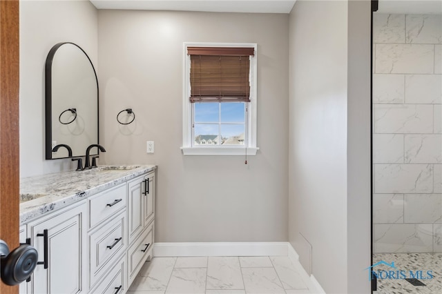 full bath with marble finish floor, a tile shower, vanity, and baseboards