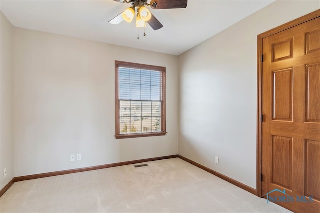 spare room with a ceiling fan, light colored carpet, visible vents, and baseboards