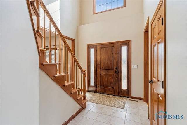 entrance foyer with baseboards, visible vents, stairs, a high ceiling, and light tile patterned flooring