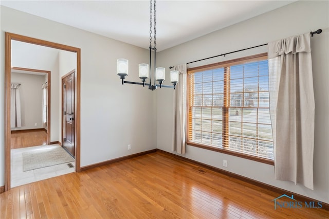 unfurnished dining area featuring baseboards, an inviting chandelier, visible vents, and light wood-style floors