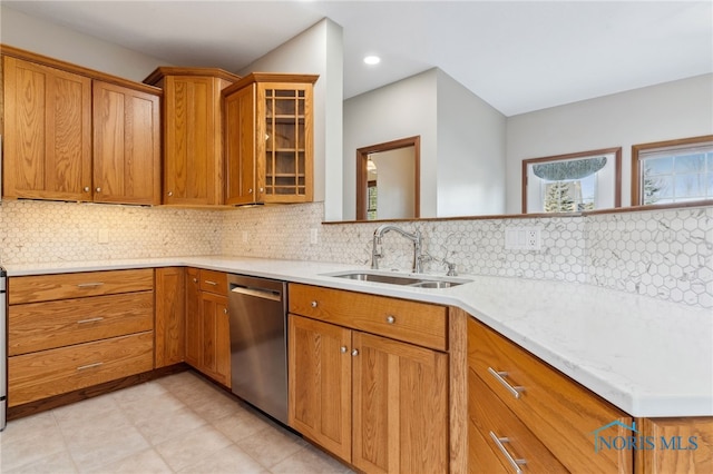 kitchen with a sink, stainless steel dishwasher, tasteful backsplash, brown cabinetry, and glass insert cabinets