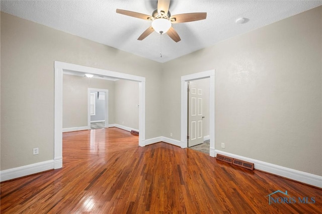 empty room featuring a textured ceiling, wood finished floors, visible vents, and baseboards