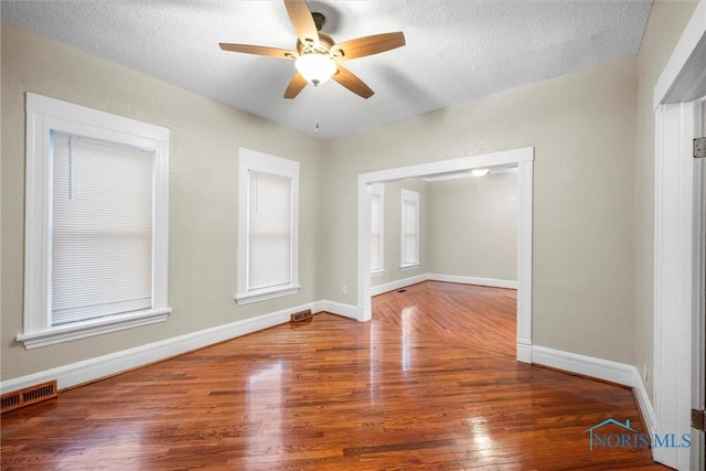 empty room with baseboards, a textured ceiling, visible vents, and wood finished floors