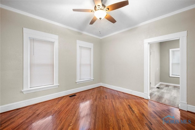 spare room with baseboards, wood finished floors, visible vents, and crown molding