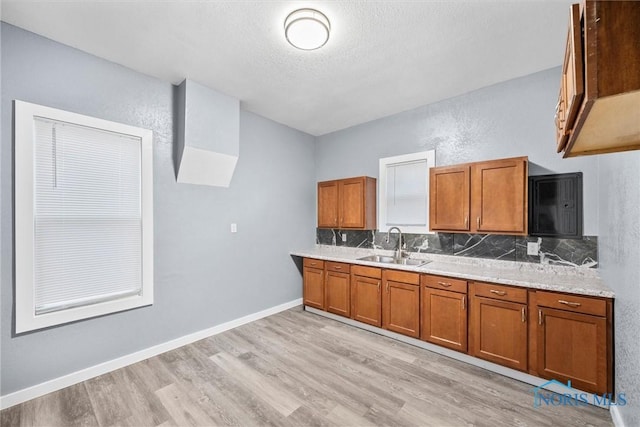 kitchen with baseboards, light wood-style flooring, brown cabinets, light countertops, and a sink