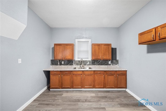 kitchen with light wood finished floors, brown cabinetry, a sink, and baseboards