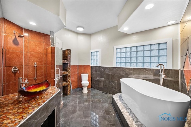 full bath with tile walls, marble finish floor, a freestanding bath, a sink, and recessed lighting