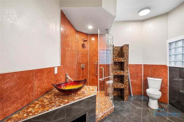 full bath with tiled shower, toilet, marble finish floor, vanity, and tile walls