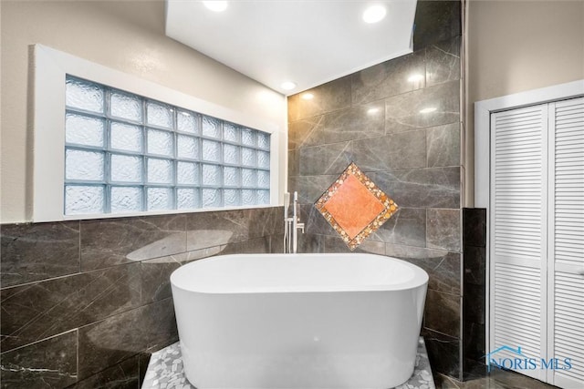 bathroom featuring recessed lighting, a closet, a freestanding bath, and tile walls