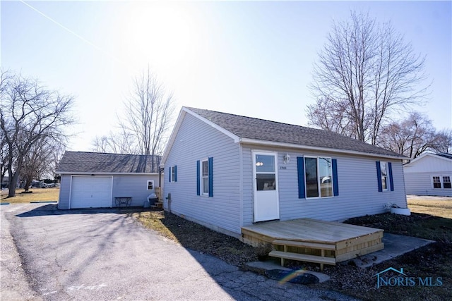 view of front of house with an outbuilding, a wooden deck, a garage, and roof with shingles