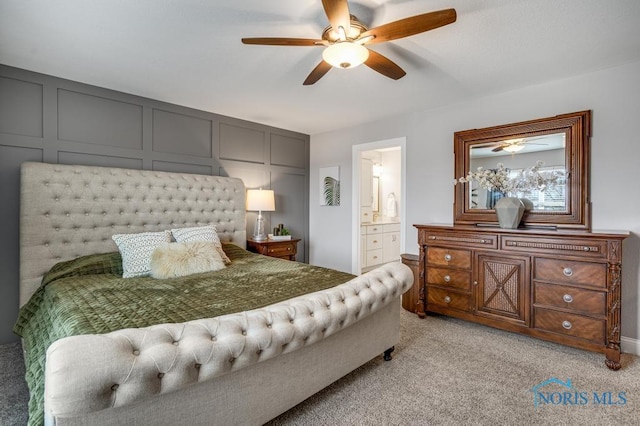 bedroom with ensuite bathroom, a decorative wall, a ceiling fan, and light colored carpet