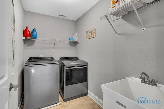 clothes washing area with visible vents, a sink, washer and dryer, laundry area, and baseboards