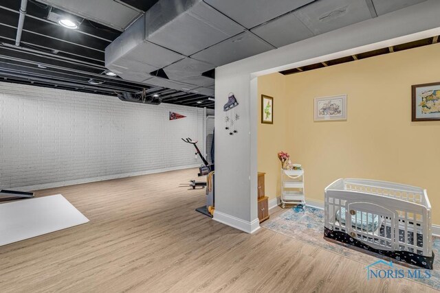 exercise room with baseboards, brick wall, and wood finished floors