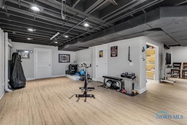 exercise area featuring brick wall, baseboards, and wood finished floors