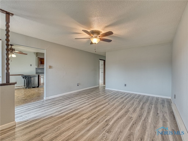 spare room featuring light wood finished floors, a textured ceiling, baseboards, and a ceiling fan