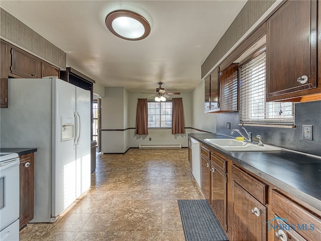 kitchen with dark countertops, a baseboard heating unit, a sink, ceiling fan, and white appliances