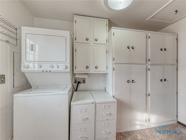 washroom with stacked washer and dryer, cabinet space, and a textured ceiling