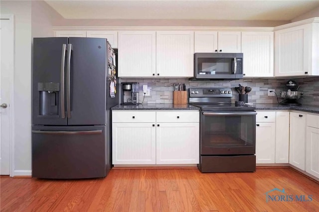 kitchen featuring stainless steel appliances, tasteful backsplash, white cabinetry, dark stone countertops, and light wood-type flooring