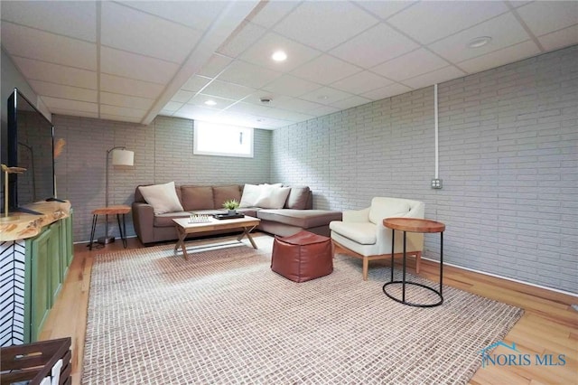 living area featuring brick wall, wood finished floors, and a paneled ceiling