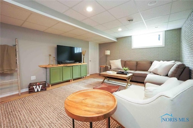 living room featuring baseboards, brick wall, light wood-style flooring, a paneled ceiling, and recessed lighting