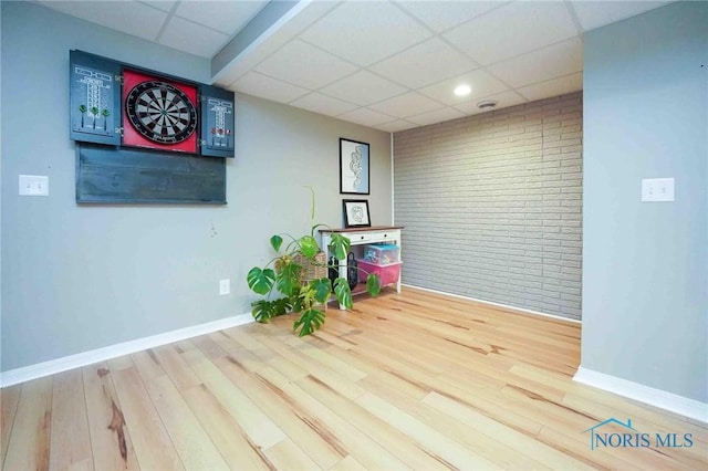 spare room featuring a paneled ceiling, baseboards, brick wall, and wood finished floors