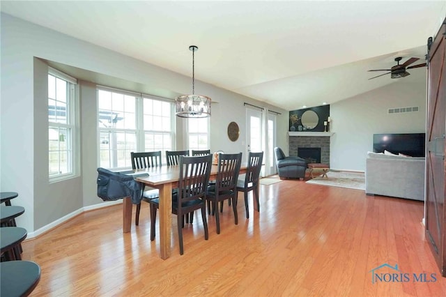 dining space with lofted ceiling, light wood-type flooring, visible vents, and a brick fireplace