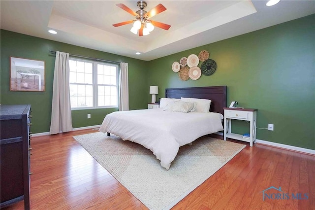 bedroom with baseboards, a raised ceiling, wood finished floors, and recessed lighting