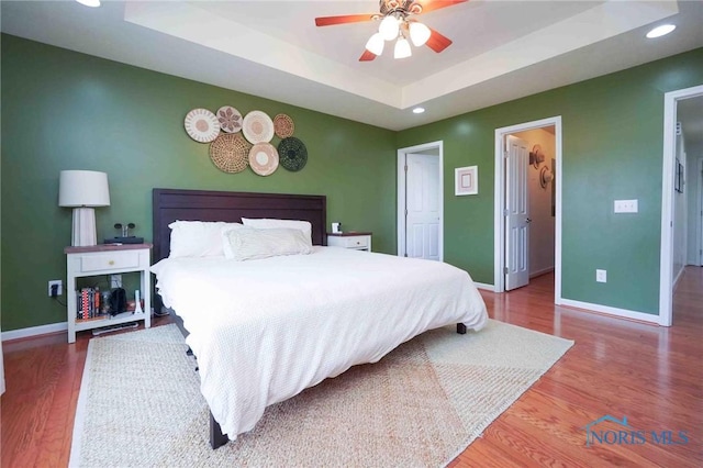 bedroom featuring recessed lighting, wood finished floors, baseboards, a walk in closet, and a raised ceiling