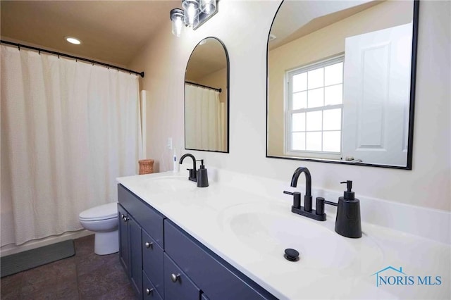 full bath featuring double vanity, a shower with curtain, toilet, and a sink