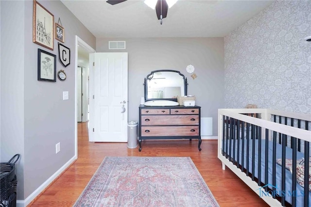 bedroom with an accent wall, wood finished floors, visible vents, and wallpapered walls