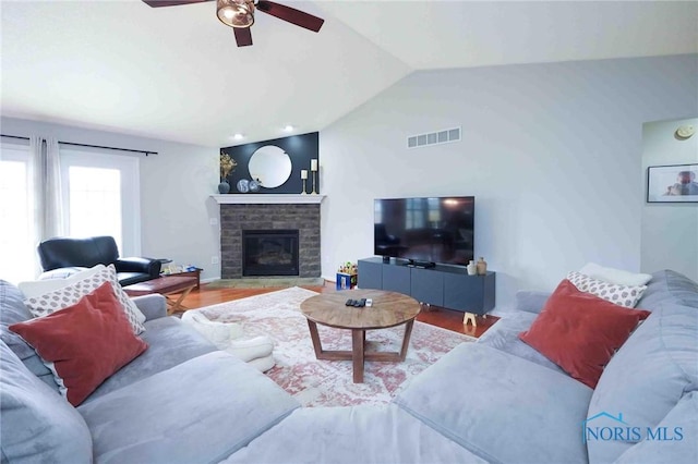 living room with lofted ceiling, visible vents, a ceiling fan, a brick fireplace, and wood finished floors