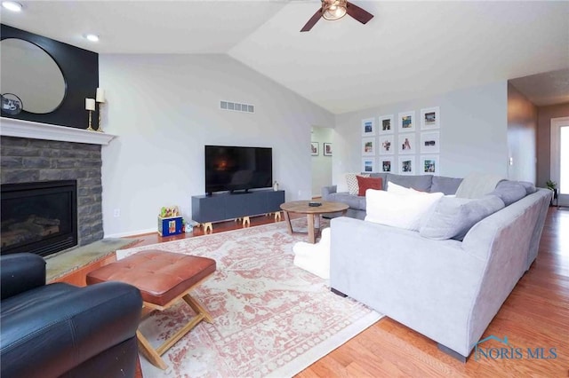 living area featuring ceiling fan, wood finished floors, visible vents, vaulted ceiling, and a glass covered fireplace