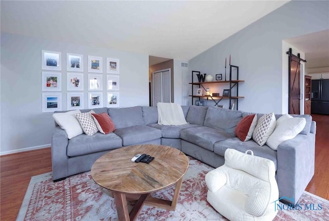 living area with a barn door, baseboards, vaulted ceiling, and wood finished floors