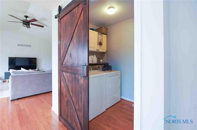 washroom with a barn door, separate washer and dryer, visible vents, light wood-type flooring, and cabinet space