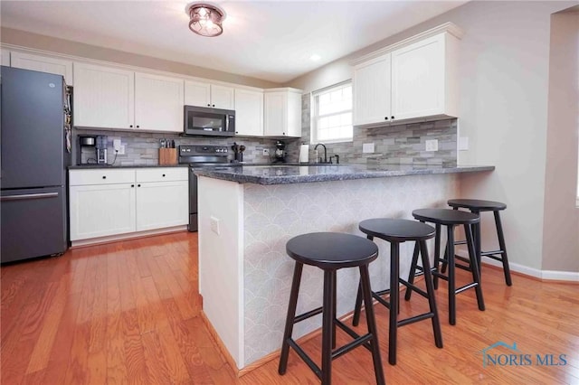 kitchen featuring black appliances, light wood-style flooring, a kitchen bar, and white cabinetry