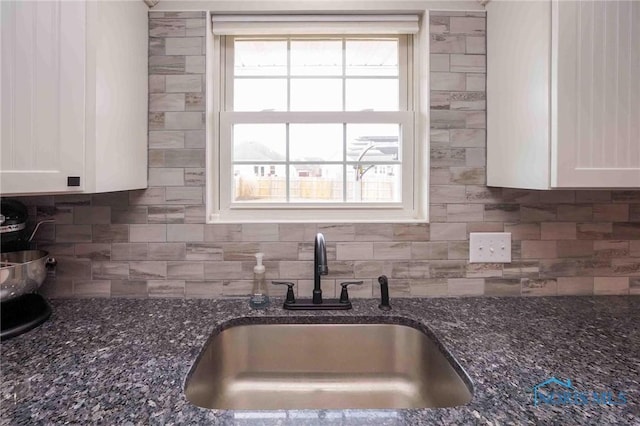 kitchen featuring dark stone counters, backsplash, a sink, and white cabinets