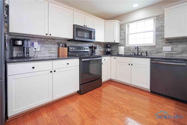 kitchen with a sink, white cabinets, appliances with stainless steel finishes, light wood-type flooring, and dark stone countertops