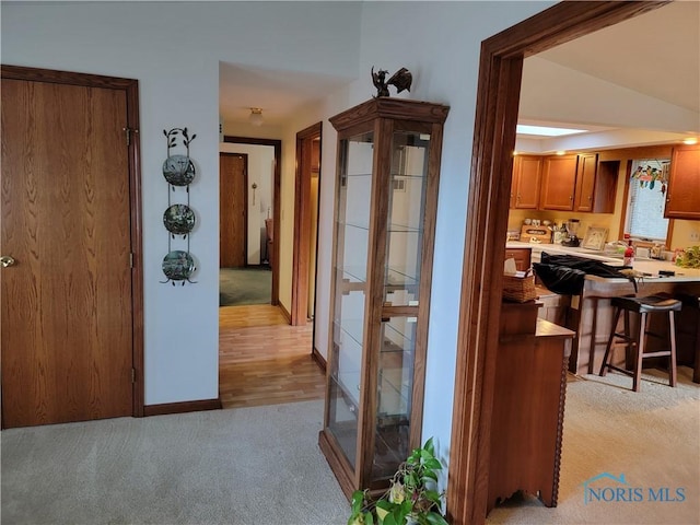 hall with lofted ceiling, light colored carpet, and baseboards