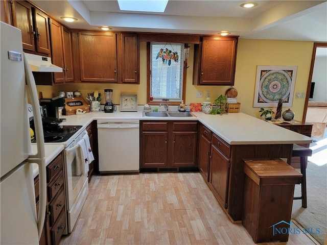 kitchen featuring white appliances, a peninsula, under cabinet range hood, a kitchen bar, and a sink