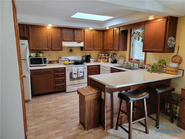 kitchen featuring light countertops, a sink, white appliances, a peninsula, and under cabinet range hood