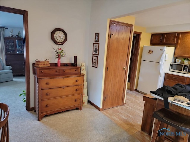 kitchen with light colored carpet, freestanding refrigerator, stainless steel microwave, and baseboards