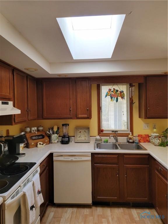 kitchen with white appliances, light wood-style floors, light countertops, under cabinet range hood, and a sink