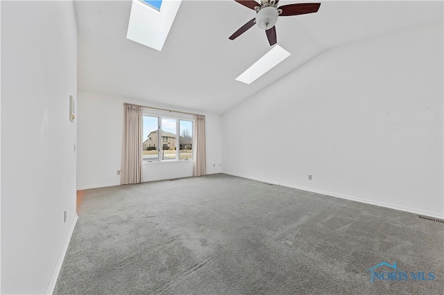 interior space featuring ceiling fan, vaulted ceiling with skylight, visible vents, and baseboards