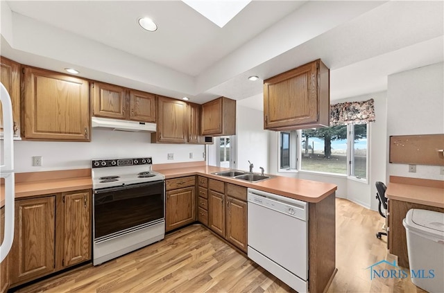 kitchen featuring white appliances, light wood finished floors, a peninsula, under cabinet range hood, and a sink