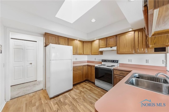 kitchen with under cabinet range hood, white appliances, a skylight, a sink, and light wood-type flooring