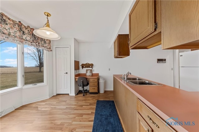 kitchen with light wood-style flooring, a sink, light countertops, freestanding refrigerator, and decorative light fixtures